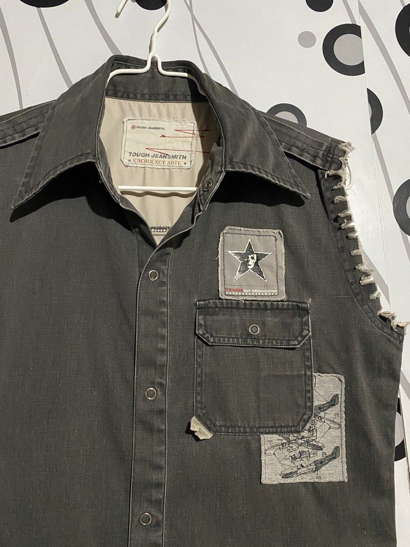 Vintage Tough Jeansmith sleeveless (Category: Tshirts & Polo Shirts ) located in Cebu City. Submitted by patspickph (Listing ID 1463261601, Image 3). Description: This is a vintage Tough Jeansmith sleeveless military-style or utility button-down shirt, likely from the Y2K era. Features the distinctive "Tough Jeansmith Emergency Note" collar and neck branding tag. **Details: Dark charcoal grey cotton fabric, snap buttons, a chest pocket with a sta