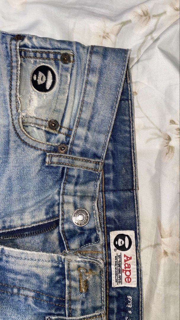 AAPE BY A BATHING APE® Jeans (Category: Jeans) located in Manila. Submitted by saintino0222 (Listing ID 1463333349, Image 2). Description: - Light wash denim jeans from AAPE BY A BATHING APE® - Signature ape head logo on coin pocket - Embroidered details on back pockets - Distressing and fading throughout for a worn-in look - Red and blue stripe detail with AAPE branding on cuffs.