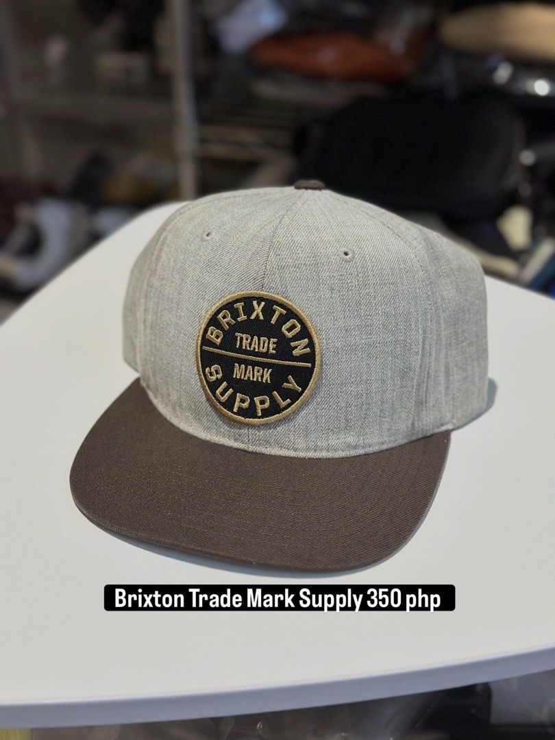 Brixton Trade Mark Supply Snapback Hat (Category: Caps & Hats) located in Daet. Submitted by thrifthings2018 (Listing ID 1463425275, Image 1). Description: - Brand: Brixton - Style: Snapback hat - Colors: Grey and brown - Features: 'Brixton Trade Mark Supply' logo patch on front - Fit: Adjustable strap at the back - Design: Classic flat brim - Ideal for: Everyday wear.