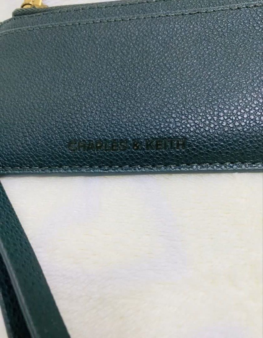 Charles & Keith Card Holder with Wrist Strap (Category: Wallets & Card holders) located in Manila. Submitted by TindahanNiLhelay (Listing ID 1463329450, Image 2). Description: - Dark green Charles & Keith card holder - Textured leather-look finish - Multiple card slots on the front - Secure side zipper closure - Includes a detachable wrist strap - Adorned with a gold charm - Ideal for keeping your cards organized and accessible.