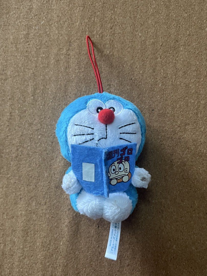 Doraemon Plush Keychain Reading Book (Category: Plushies & Soft Toys) located in Baguio. Submitted by gaara1234 (Listing ID 1463350694, Image 1). Description: - Adorable Doraemon plush keychain - Features a mini book accessory with 'Weekly Goro' text - Made in China for amusement purposes - Includes a red string loop for easy hanging - Ideal for decorating bags, backpacks, or keys.