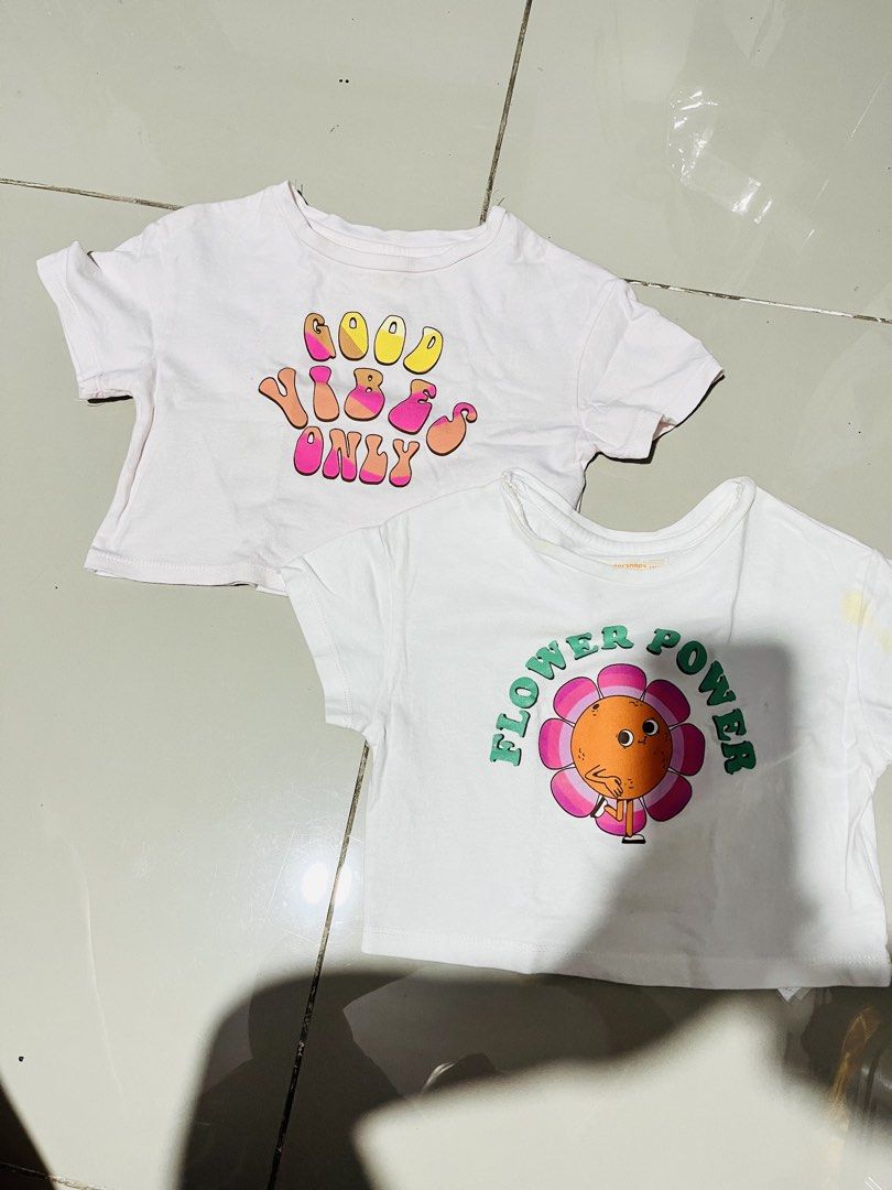 Gingersnaps Top (Category: Babies & Kids Fashion) located in Manila. Submitted by islaalon525 (Listing ID 1463337368, Image 1). Description: - Two cute white crop tops for girls. - One features a 'Good Vibes Only' graphic in groovy lettering. - The other has a 'Flower Power' design with a smiling flower. - Both are short-sleeved and cropped style. - Great for casual wear or layering. - Adds a fun touch to any outfit..