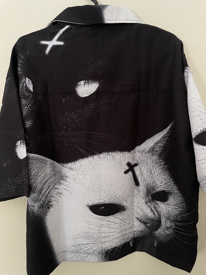 DGRAVE Polo Shirt (Category: Tshirts & Polo Shirts ) located in Manila. Submitted by kristinamaria (Listing ID 1463340313, Image 2). Description: - Unique black and white graphic shirt - Features a cat and cross design - Short sleeves - Button-up front - All-over print - Estimated size Medium/Large (check measurements for best fit) - Perfect statement piece.