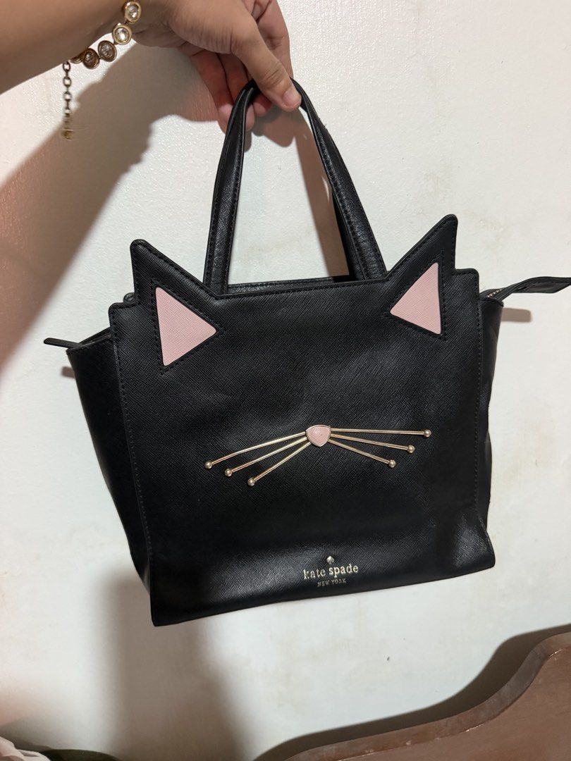 Kate Spade Black Cat Face Tote Bag (Category: Tote Bags) located in San Pablo. Submitted by prelovedbymistyblue (Listing ID 1463387237, Image 1). Description: - Cute black Kate Spade tote bag - Features playful pink cat ears and whiskers detail - Secure top zip closure - Sturdy and reliable handles - Spacious interior for all your essentials - Ideal for everyday use or as a unique statement piece With sling slot but no strap included, with rubber