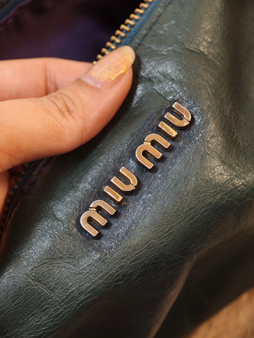 Miu Miu kili bag (Category: Luxury Bags & Wallets) located in Don Carlos. Submitted by thejoyofbags2 (Listing ID 1463368847, Image 3). Description: - Dark green Miu Miu shoulder bag - Made from soft, crinkled leather - Zip closure - Cute bow detail on the side - Adjustable strap with gold hardware - Shows some signs of wear on leather and strap, consistent with use - Stylish everyday bag.