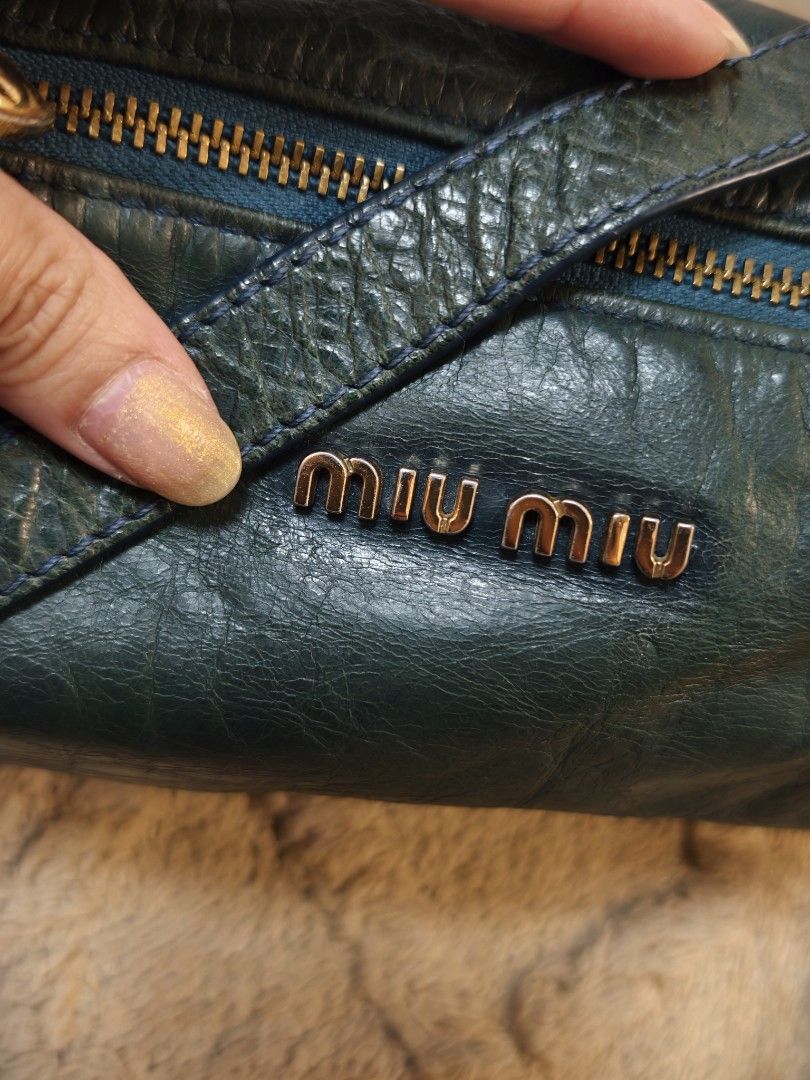 Miu Miu kili bag (Category: Luxury Bags & Wallets) located in Don Carlos. Submitted by thejoyofbags2 (Listing ID 1463368847, Image 2). Description: - Dark green Miu Miu shoulder bag - Made from soft, crinkled leather - Zip closure - Cute bow detail on the side - Adjustable strap with gold hardware - Shows some signs of wear on leather and strap, consistent with use - Stylish everyday bag.