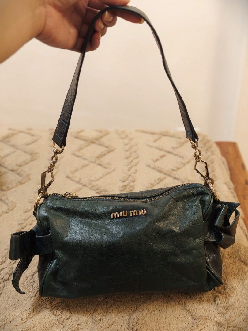 Miu Miu kili bag (Category: Luxury Bags & Wallets) located in Don Carlos. Submitted by thejoyofbags2 (Listing ID 1463368847, Image 1). Description: - Dark green Miu Miu shoulder bag - Made from soft, crinkled leather - Zip closure - Cute bow detail on the side - Adjustable strap with gold hardware - Shows some signs of wear on leather and strap, consistent with use - Stylish everyday bag.