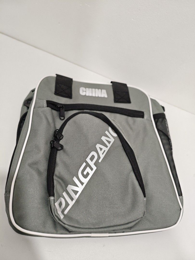 Pingpang Table Tennis Racket Bag Shoulder Bag (Category: Racket and Ball Sports) located in San Jose del Monte. Submitted by jenmallari_ (Listing ID 1463554982, Image 1). Description: - Grey racket bag with 'CHINA' and 'PINGPANG' branding. - Main compartment for rackets and accessories. - Front pocket for smaller items. - Side mesh pockets for water bottles or other essentials. - Versatile carrying options: top handles or adjustable shoulder stra