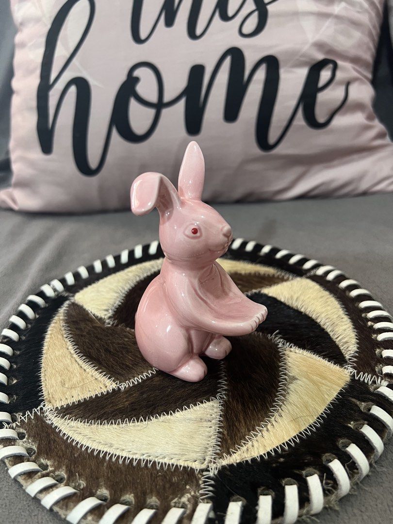 Pink Ceramic Bunny Figurine on Decorative Coaster (Category: Other Home Decor) located in Las Pinas. Submitted by maple0305 (Listing ID 1463347350, Image 3). Description: - Cute pink ceramic bunny figurine - Sits on a unique round coaster made of patchwork animal hide - Striped trim on the coaster adds a stylish detail - Ideal for Easter decorations or as a charming shelf accent - Brings a whimsical touch to any room - Approximately 4 inches in h