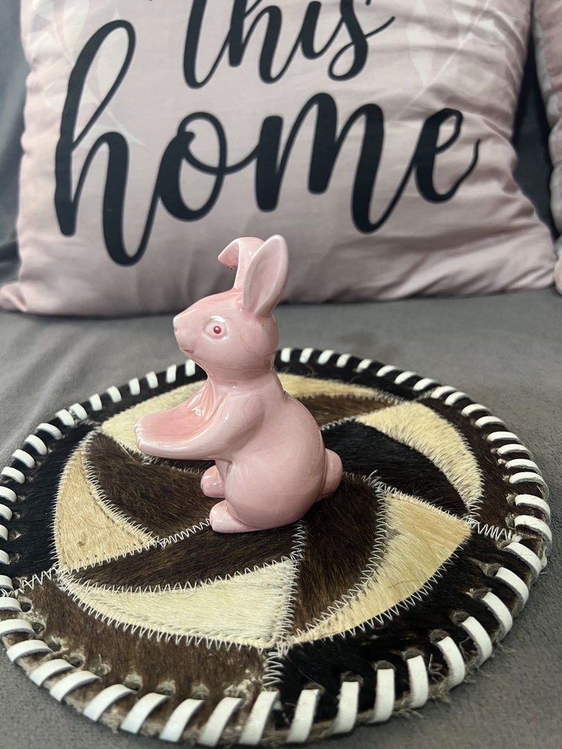 Pink Ceramic Bunny Figurine on Decorative Coaster (Category: Other Home Decor) located in Las Pinas. Submitted by maple0305 (Listing ID 1463347350, Image 2). Description: - Cute pink ceramic bunny figurine - Sits on a unique round coaster made of patchwork animal hide - Striped trim on the coaster adds a stylish detail - Ideal for Easter decorations or as a charming shelf accent - Brings a whimsical touch to any room - Approximately 4 inches in h