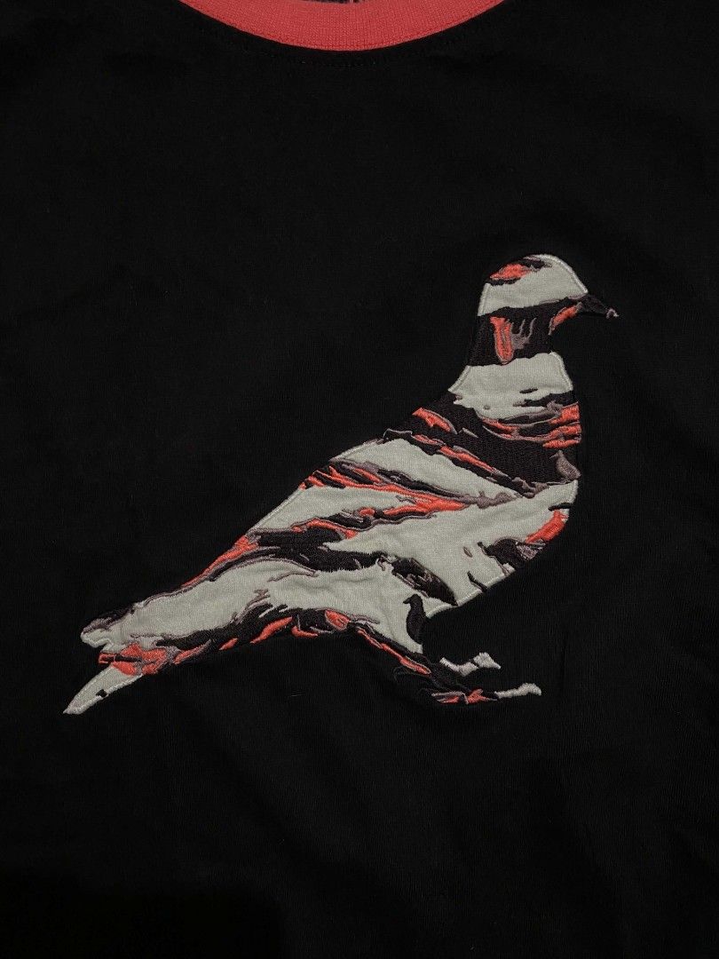 Staple "Pigeon " tee (Category: Tshirts & Polo Shirts ) located in Aroroy. Submitted by dr0p-a-dr1p (Listing ID 1463431230, Image 3). Description: - Brand: Staple - Color: Black with light blue sleeves and orange collar - Graphic: Unique abstract pigeon design in grey, black, and orange - Material: 100% Cotton - Size: Medium (M) - Style: Casual wear.