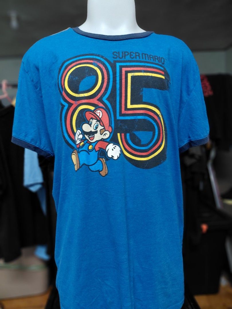 Super Mario 85 Blue T-shirt (Category: Tshirts & Polo Shirts ) located in Baguio. Submitted by undressme24 (Listing ID 1463497893, Image 1). Description: Blue t-shirt with a Super Mario 85 graphic. Features Mario running with the number 85 in bold colors. Ringer tee style with navy blue trim on the collar and sleeves. Great for any Mario fan. Comfortable and casual wear. .