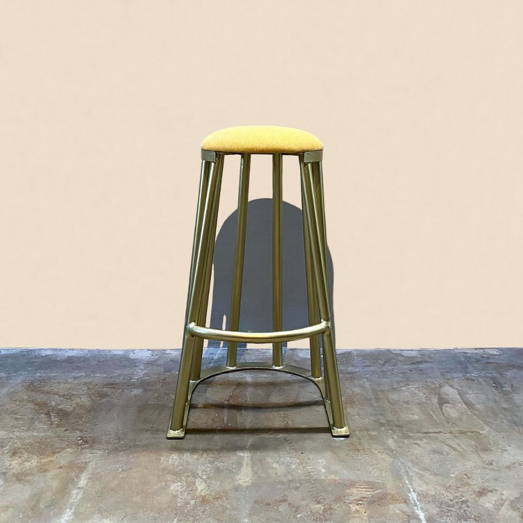 Tanzan Counter Stool (Category: Chairs) located in Paranaque City. Submitted by furniturepiecesph (Listing ID 1463369580, Image 1). Description: This Tanzan Counter Stool, balances a minimalist silhouette with striking sculptural textures. Features a thick, rounded yellow cushion covered in a textured fabric, ensuring a comfortable sit. Cage-Like Base: Built from curved gold-finished metal rods that form a rhythmic vertical cage pattern, resting 