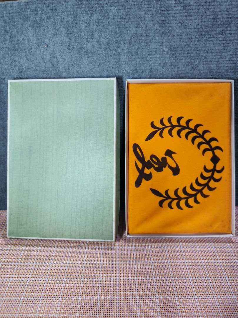 Vintage Boxed Item with Orange Fabric Insert (Category: Other Home Decor) located in San Leonardo. Submitted by burgossanleonardo.12345 (Listing ID 1463455107, Image 2). Description: - Comes with a light green box. - Includes an orange fabric insert with a black laurel wreath design and script text. - Item has been stored in the box. - Selling as is..