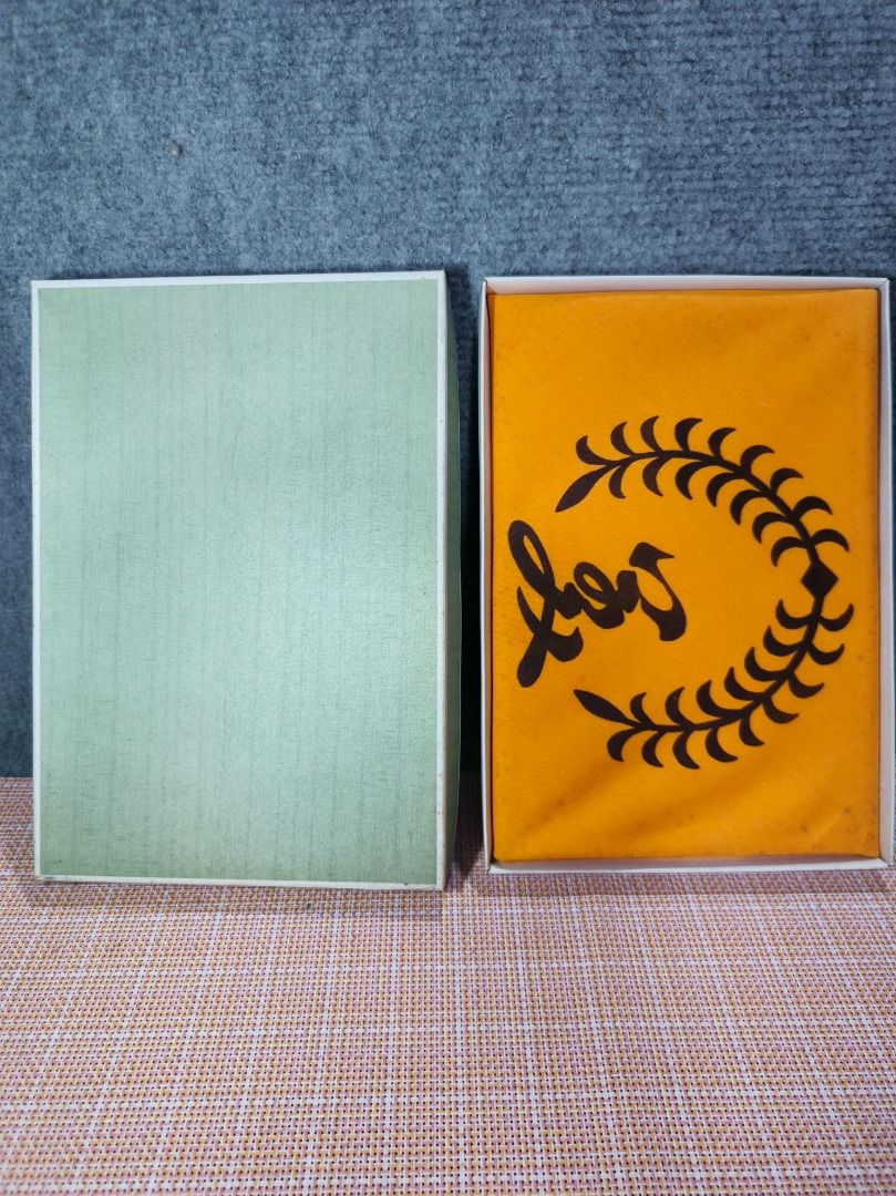 Vintage Boxed Item with Orange Fabric Insert (Category: Other Home Decor) located in San Leonardo. Submitted by burgossanleonardo.12345 (Listing ID 1463455107, Image 1). Description: - Comes with a light green box. - Includes an orange fabric insert with a black laurel wreath design and script text. - Item has been stored in the box. - Selling as is..