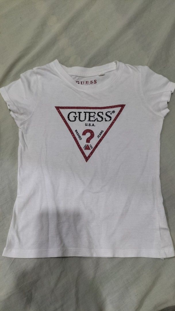 White Guess T-shirt with Sequined Logo (Category: Babies & Kids Fashion) located in Angeles City. Submitted by morikori (Listing ID 1463399784, Image 1). Description: - size: 6 years old - White Guess t-shirt - Features iconic red and black sequined triangle logo - 'Guess U.S.A.' and 'Washed 1201 Jeans 1203' detail - Short sleeves - Classic crew neck - Ideal for casual wear.