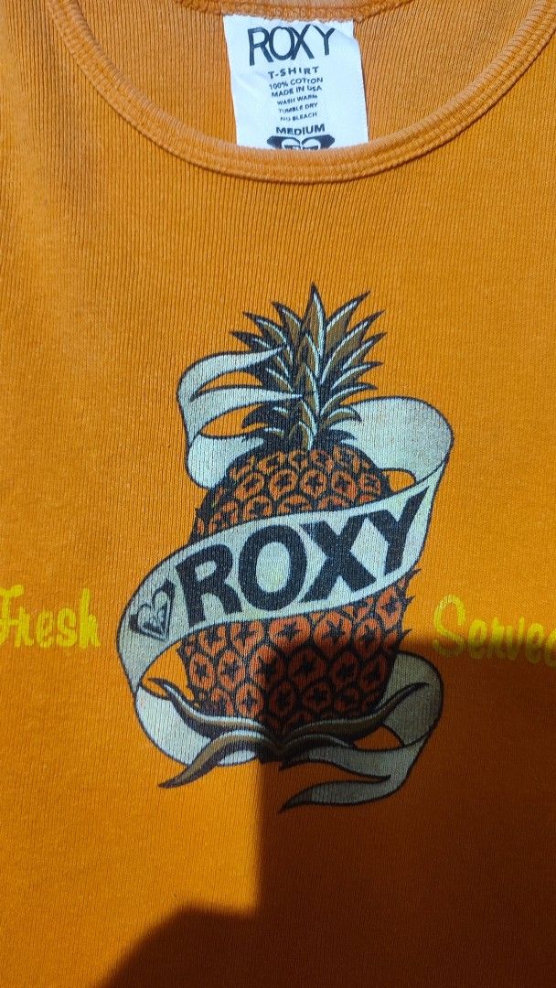 Y2k Roxy Orange Pineapple Graphic Tank Top (Category: Sleeveless) located in Zamboanga. Submitted by archivist_ (Listing ID 1463399459, Image 2). Description: - Cute orange Roxy tank top - Features a fun pineapple graphic - Roxy logo and 'Cut Fresh Served Sweet' text - Ribbed texture - Ideal for casual wear or beach days Issue: Faded.