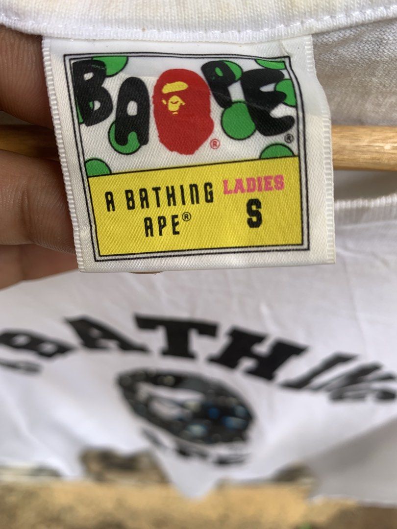 A Bathing Ape Ladies Tee Size S White BAPE (Category: Shirts) located in Aloran. Submitted by chester78864 (Listing ID 1463657870, Image 3). Description: - Authentic White A Bathing Ape (BAPE) T- -with sign of use. minir stain and need wash Shirt - Features the classic BAPE ape head logo with a camouflage pattern - Ladies Size S - Ideal for any BAPE enthusiast - Please check photos for detailed condition.