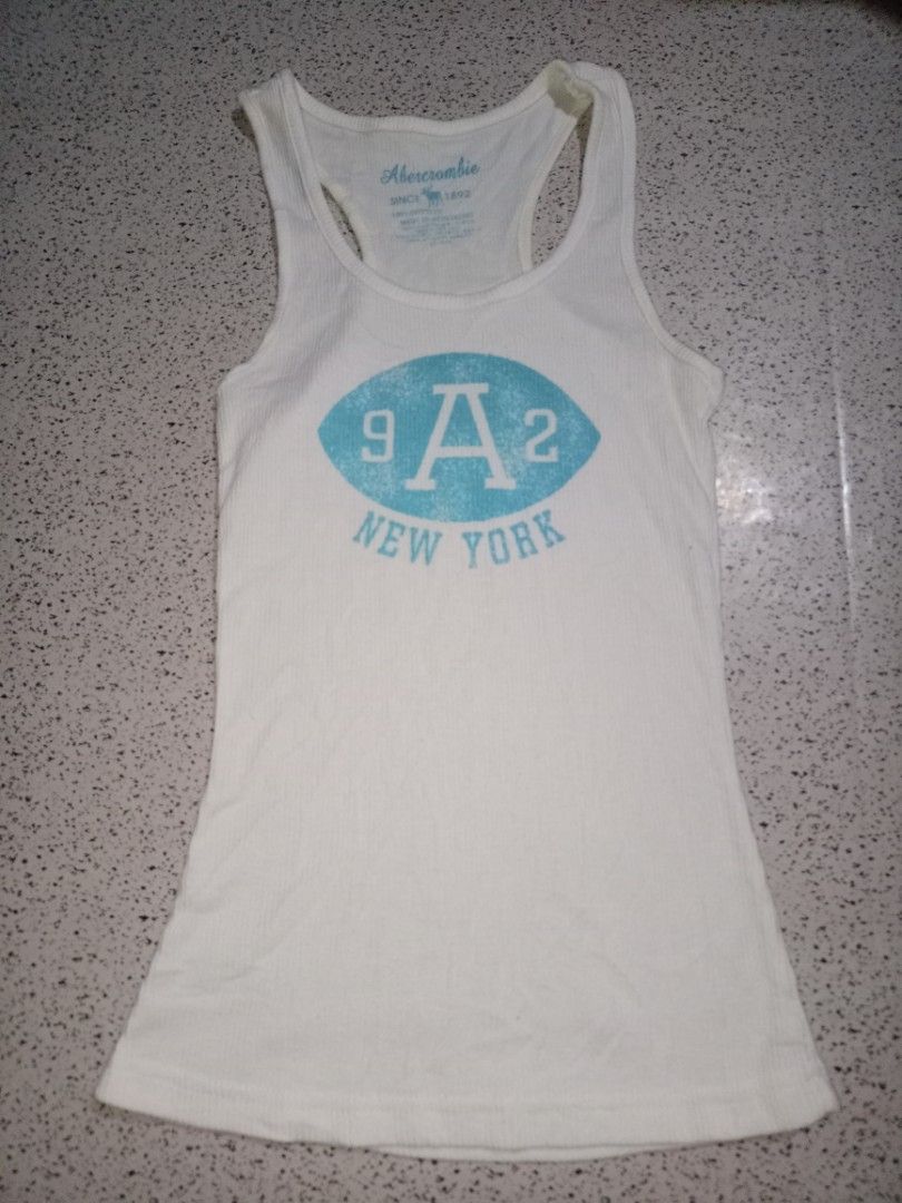 Abercrombie New York Graphic Tank Top (Category: Sleeveless) located in Caloocan City. Submitted by elle_f08 (Listing ID 1463667149, Image 1). Description: - White ribbed tank top from Abercrombie - Features '9A2 New York' graphic in blue on the front - Made of 100% cotton - Ideal for casual wear.
