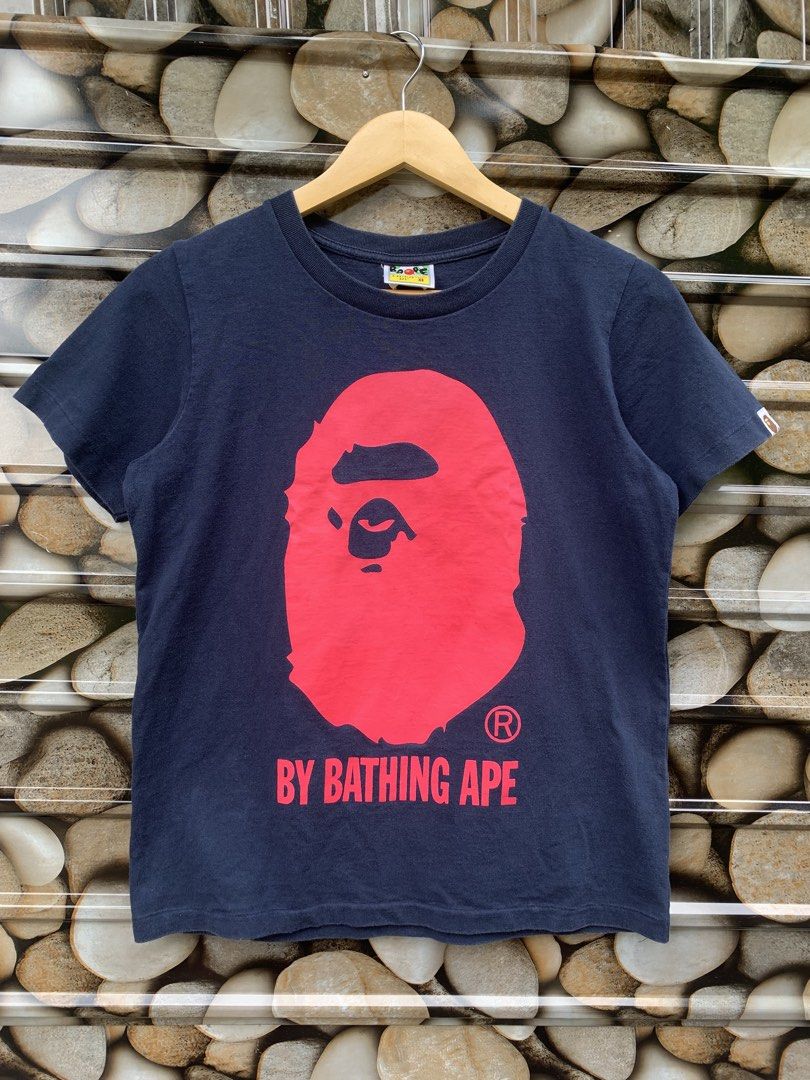 BAPE Big Head XS (Category: Tshirts & Polo Shirts ) located in Aloran. Submitted by chester78864 (Listing ID 1463658272, Image 1). Description: - Navy blue BAPE t-shirt - Iconic red ape head graphic - Text reads 'BY BATHING APE' - Tagged as 'A BATHING APE LADIES XS' - Small brown ape head tag on sleeve - Ideal for streetwear enthusiasts.