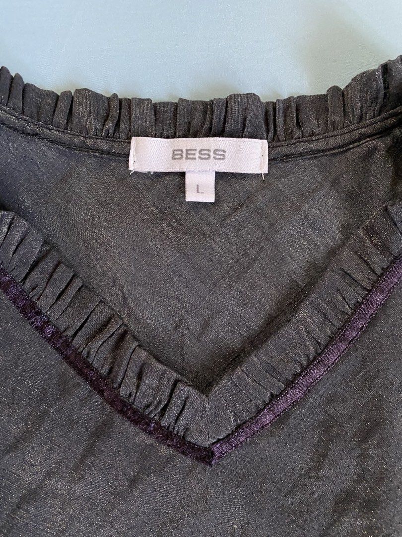 Bess Metallic Grey Ruffled V-Neck Top (Category: Sleeveless) located in Manila. Submitted by heyheyruok (Listing ID 1463611870, Image 3). Description: - Brand: BESS - Color: Dark Grey - Size: L - Neckline: Ruffled V-neck with dark trim - Sleeves: Long sleeves with ruffled cuffs and dark trim - Fabric: Subtle sheen and texture - Occasion: Suitable for casual or slightly dressier events - Much prettier in person! - Not stretchable - Perfect for off