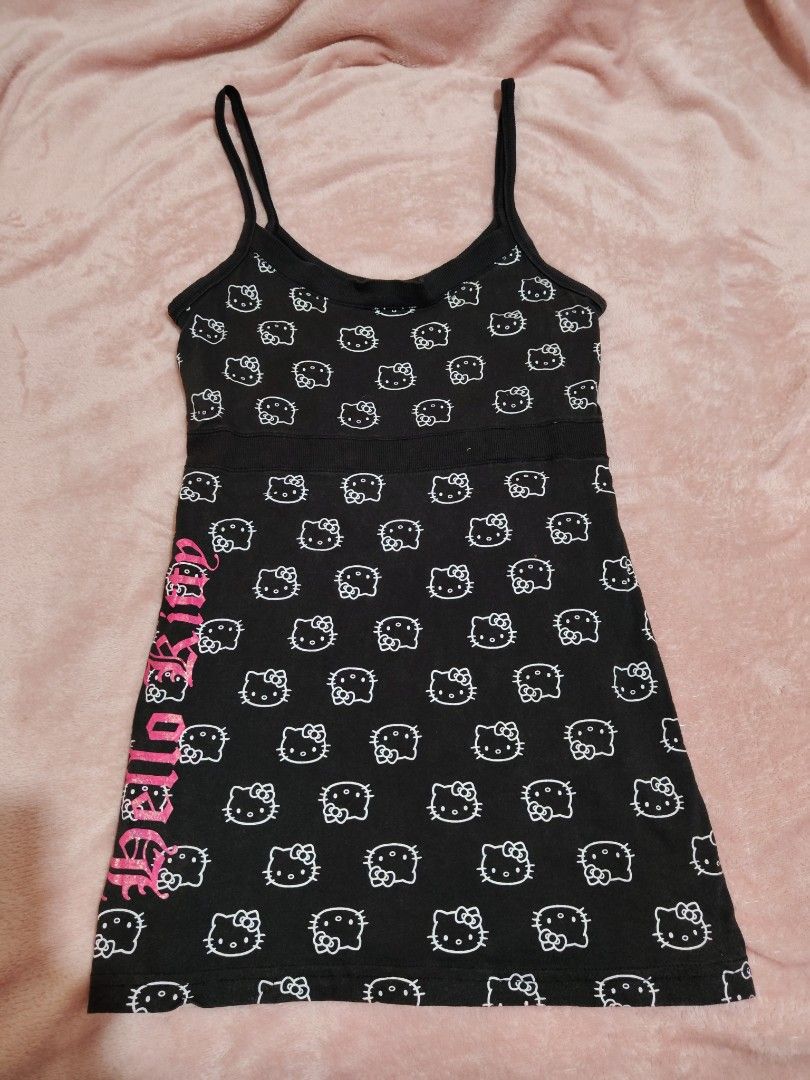 Black Hello Kitty All Over Print Babydoll Top (Category: Sleeveless) located in Villasis. Submitted by trip_thrift15 (Listing ID 1463666834, Image 1). Description: - Adorable black tank top with an all-over white Kitty print. - Features a vibrant hot pink ' Kitty' graphic down the side. - Comfortable spaghetti straps for a relaxed fit. - Made from soft, comfortable fabric. - Officially licensed by Sanrio and Blues Clothing. - Ideal for casual out