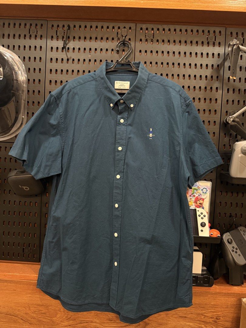 GIORDANO Men's Short Sleeve Button Down Shirt (Category: Tshirts & Polo Shirts ) located in San Fernando. Submitted by archvst.selects (Listing ID 1463669100, Image 1). Description: - Dark blue short sleeve button down shirt - Brand: GIORDANO - Features a small embroidered bear graphic on the chest - Classic fit - Made with stretch fabric for comfort - Versatile for casual or smart casual wear - Button collar detail - Two pleats on the back for a