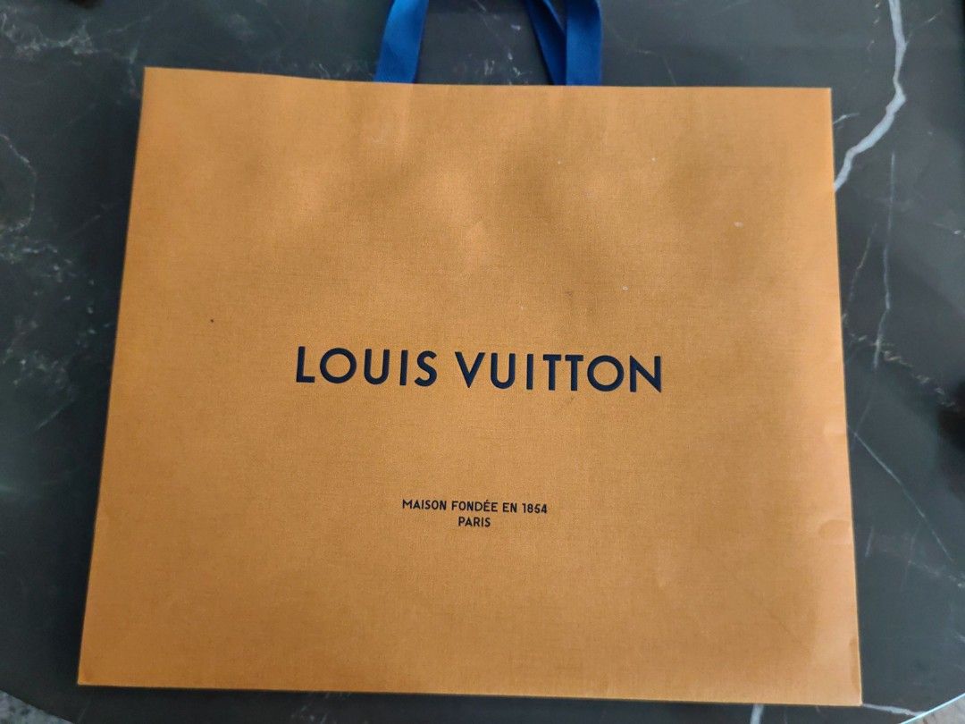 Louis Vuitton Shopping Bag (Category: Luxury Bags & Wallets) located in Makati City. Submitted by kruelscloset (Listing ID 1463602861, Image 1). Description: - Authentic Louis Vuitton paper shopping bag - Color: Orange with blue handles - Approximate dimensions: 13 inches height, length 16in - Features "Maison fondée en 1854 Paris" - Ideal for storing or gifting Louis Vuitton purchases - Condition: Clean and sturdy.
