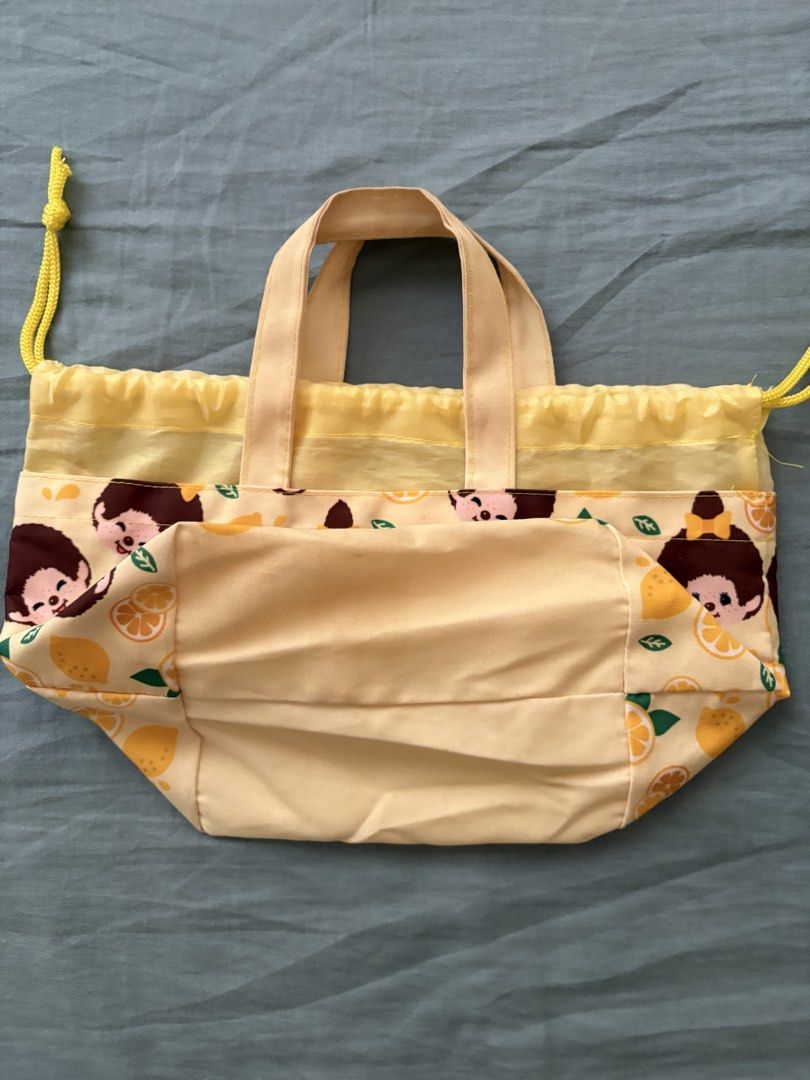 Monchhichi Lemon Print Small Drawstring Bag (Category: Tote Bags) located in Manila. Submitted by anabri (Listing ID 1463609372, Image 3). Description: - Adorable Monchhichi bag with a vibrant lemon print. - Cheerful yellow color featuring iconic Monchhichi characters. - Equipped with convenient handles for easy carrying. - Secure drawstring closure to keep contents safe. - Ideal for snacks, lunch, or storing small essentials. - Perfect for both 