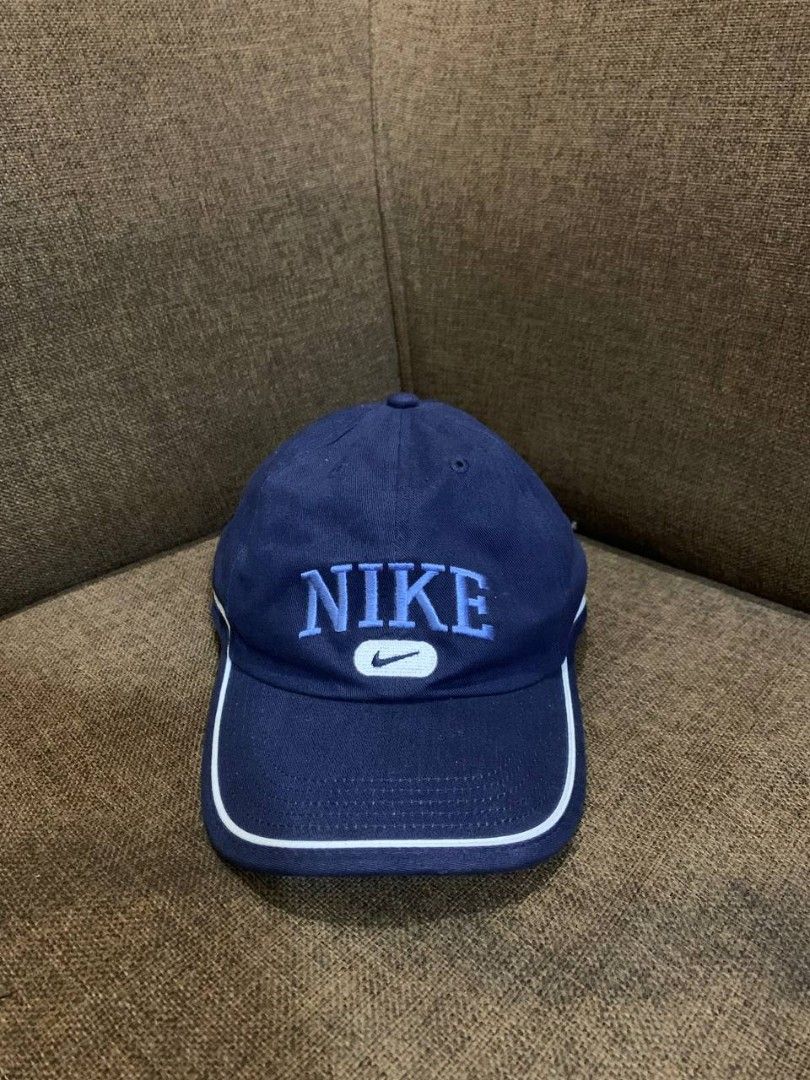 Navy Blue Nike Cap with White Trim (Category: Caps & Hats) located in Compostela. Submitted by francis_ace (Listing ID 1463663283, Image 1). Description: - Classic navy blue Nike cap - Embroidered 'NIKE' text and swoosh logo - White piping detail on brim - Adjustable strap for a custom fit - Ideal for everyday wear .