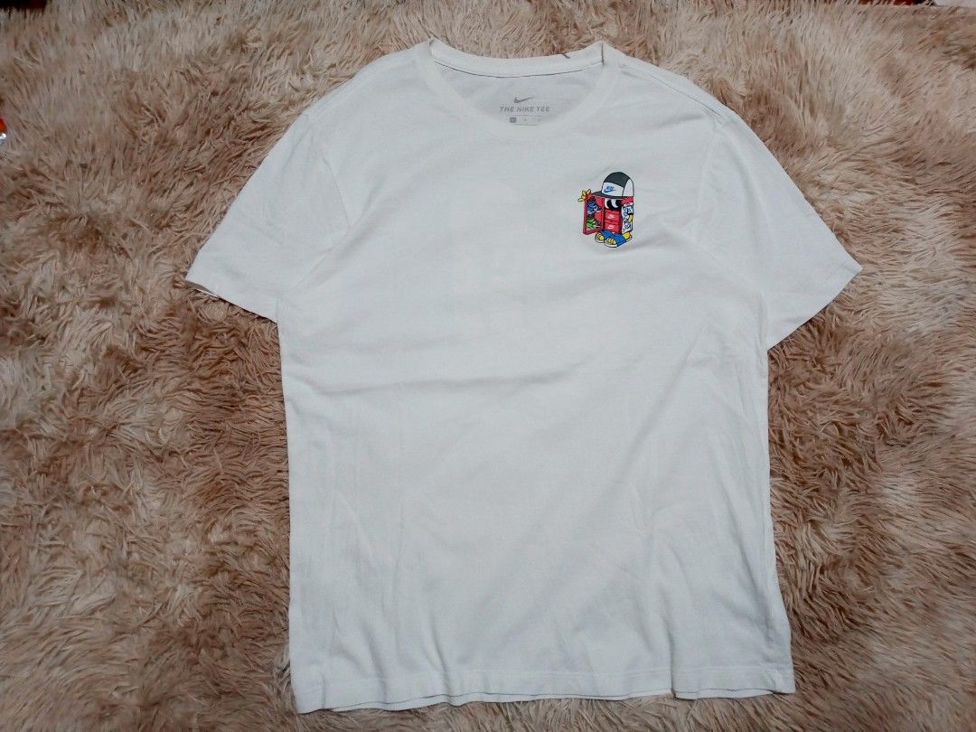 Nike Tee T-Shirt White Graphic Print (Category: Activewear) located in Boston. Submitted by johnpaulvi30029 (Listing ID 1463681769, Image 2). Description: - White Nike T-shirt - Features a fun graphic on the back with a cartoon character, sneakers, and palm trees - Small graphic on the front chest area - Nike Tee label visible on the collar - Ideal for casual wear.