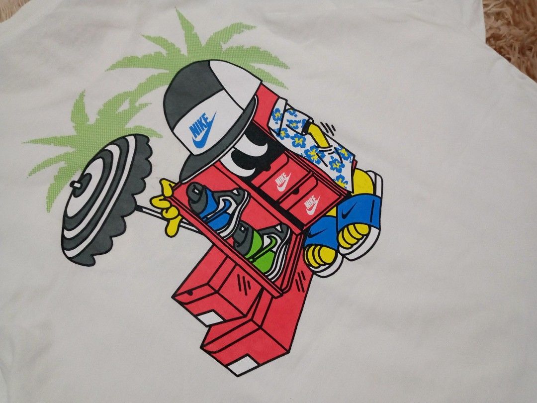 Nike Tee T-Shirt White Graphic Print (Category: Activewear) located in Boston. Submitted by johnpaulvi30029 (Listing ID 1463681769, Image 3). Description: - White Nike T-shirt - Features a fun graphic on the back with a cartoon character, sneakers, and palm trees - Small graphic on the front chest area - Nike Tee label visible on the collar - Ideal for casual wear.