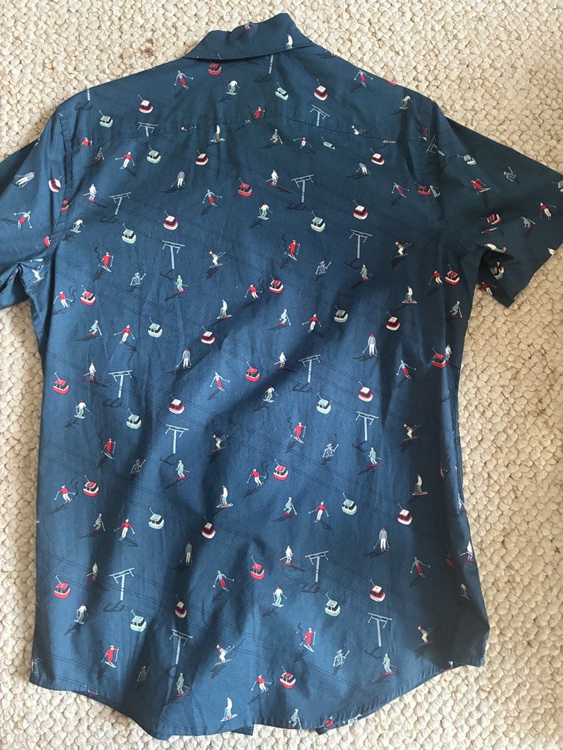 Original Penguin Short Sleeve Button Up Shirt (Category: Tshirts & Polo Shirts ) located in Cabuyao City. Submitted by chinitopoohbear (Listing ID 1463563305, Image 2). Description: - Original Penguin short sleeve button up shirt - Fun all-over print featuring skiers and ski lifts - Dark blue base color with red, white, and green accents - Button-down collar - Ideal for casual wear.