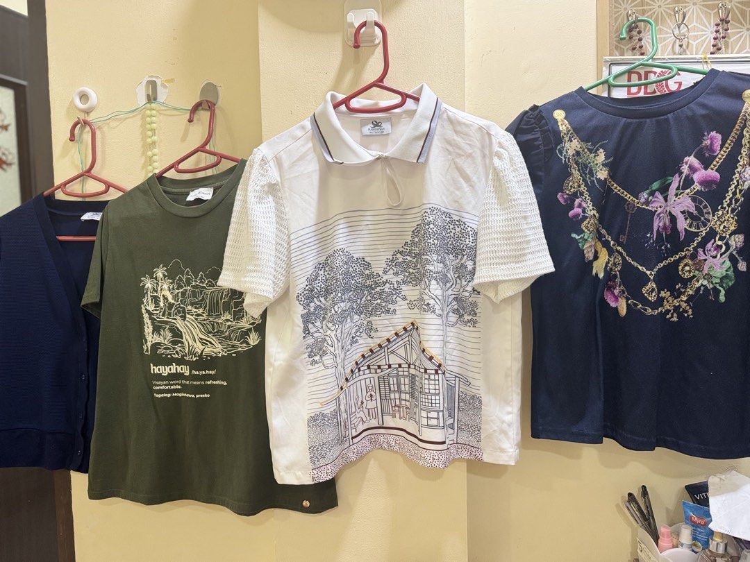 Plains and Prints Take All (Category: Blouses) located in Iba. Submitted by geliqq (Listing ID 1463636612, Image 2). Description: - Green Hayahay t-shirt featuring a unique waterfall graphic. - White collared shirt with a charming house and tree print. - Navy blue top adorned with a stylish floral and chain design on the front. - All tops are in excellent, pre-loved condition..