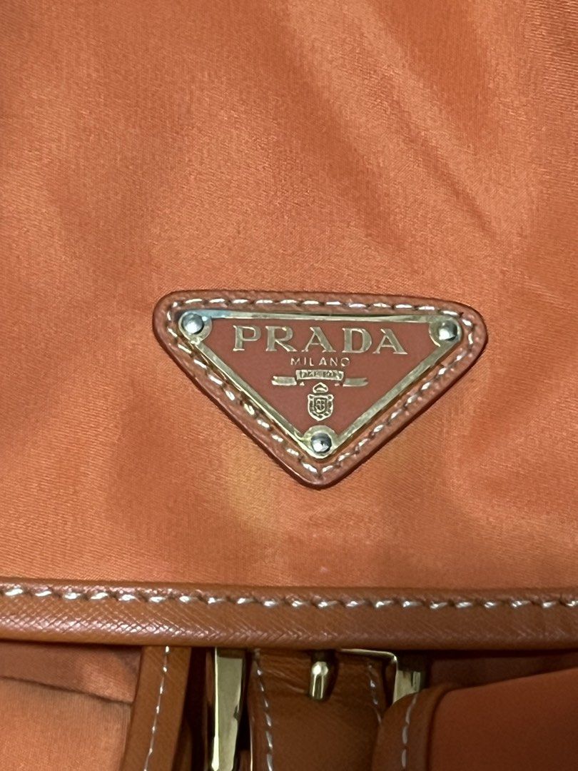 Prada Orange Nylon Leather Trim Backpack (Category: Backpacks) located in Victorias. Submitted by lan1877 (Listing ID 1463606920, Image 2). Description: - - Durable Nylon Material with Leather Trim - Elegant Gold Hardware - Convenient Front Buckle Pockets - Secure Drawstring Closure - Perfect for Everyday Use - Shows minor signs of wear on leather trim and hardware.