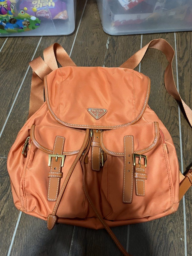 Prada Orange Nylon Leather Trim Backpack (Category: Backpacks) located in Victorias. Submitted by lan1877 (Listing ID 1463606920, Image 1). Description: - - Durable Nylon Material with Leather Trim - Elegant Gold Hardware - Convenient Front Buckle Pockets - Secure Drawstring Closure - Perfect for Everyday Use - Shows minor signs of wear on leather trim and hardware.