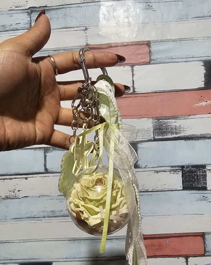 Preserved Rose bagchain with Flower Charm (Category: Charms) located in Baguio. Submitted by msgold2601 (Listing ID 1463740260, Image 2). Description: - Features a real preserved light yellow rose encased in a clear ball. - Adorned with a light green flower charm labeled 'Min'. - Includes decorative ribbons and a star charm. - Ideal for personalizing bags or keys. - A unique and charming accessory..