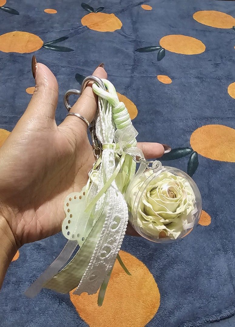 Preserved Rose bagchain with Flower Charm (Category: Charms) located in Baguio. Submitted by msgold2601 (Listing ID 1463740260, Image 3). Description: - Features a real preserved light yellow rose encased in a clear ball. - Adorned with a light green flower charm labeled 'Min'. - Includes decorative ribbons and a star charm. - Ideal for personalizing bags or keys. - A unique and charming accessory..