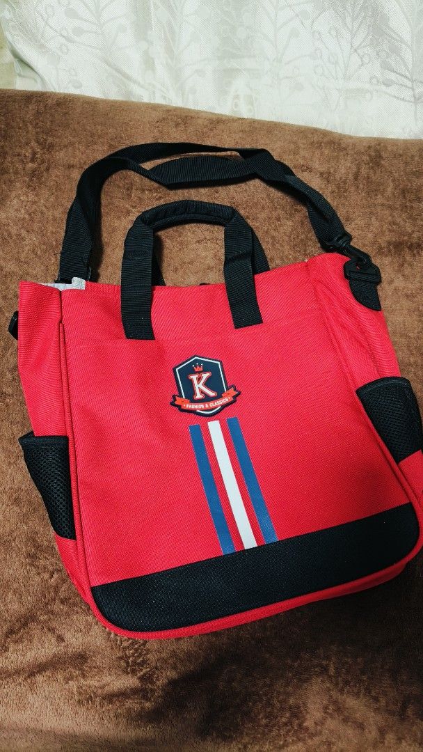 Red & Black Book Bag and Shoulder Strap (Category: Tote Bags) located in Manila. Submitted by serenitycarlylle (Listing ID 1463725593, Image 1). Description: - Eye-catching bright red tote bag - Features a prominent K logo emblem - Accented with blue and white stripes - Stylish black trim - Convenient side mesh pockets - Includes a detachable shoulder strap for versatility - Interior divider with a velcro strap for organization - Ideal for carryi