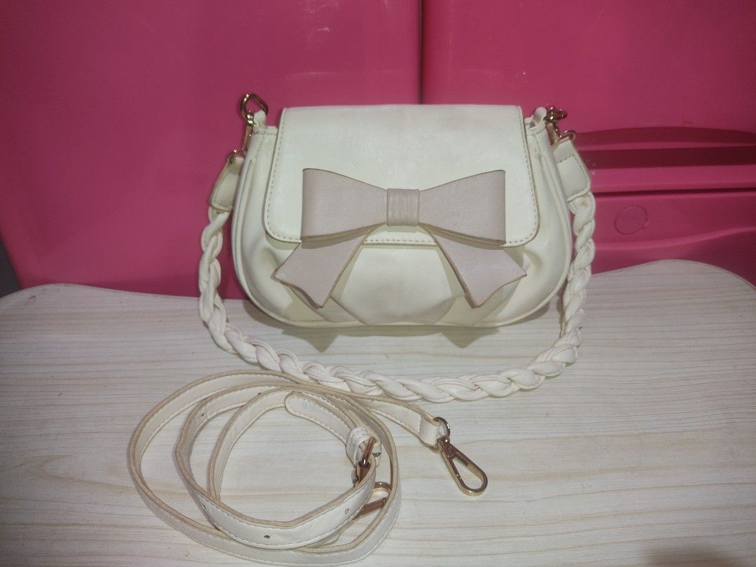 White crossbody bag with bow and braided strap (Category: Cross-body Bags) located in Manila. Submitted by xiaochao.16 (Listing ID 1463738576, Image 2). Description: - Adorable white crossbody bag - Features a sweet light pink bow on the front - Stylish braided white strap - Includes a convenient zippered pocket inside - Elegant gold hardware details - Ideal for everyday casual outings.