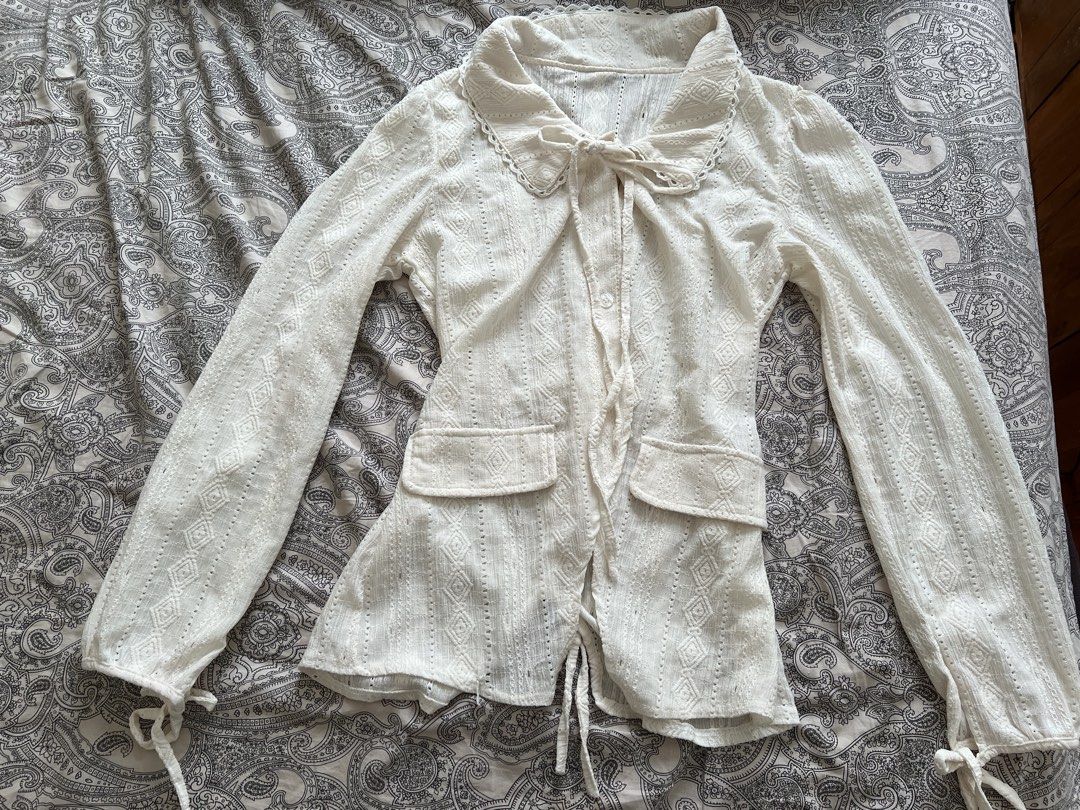 White Lace Button-Up Blouse with Tie Detail (Category: Longsleeves) located in Muntinlupa City. Submitted by sweetlovinnnnn (Listing ID 1463612521, Image 1). Description: - Elegant white long-sleeved blouse - Textured fabric with diamond and stripe patterns - Delicate lace trim on collar and cuffs - Button-up front closure - Adjustable tie details at waist and sleeves - Two functional front pockets - Estimated size: Small to Medium (S/M).