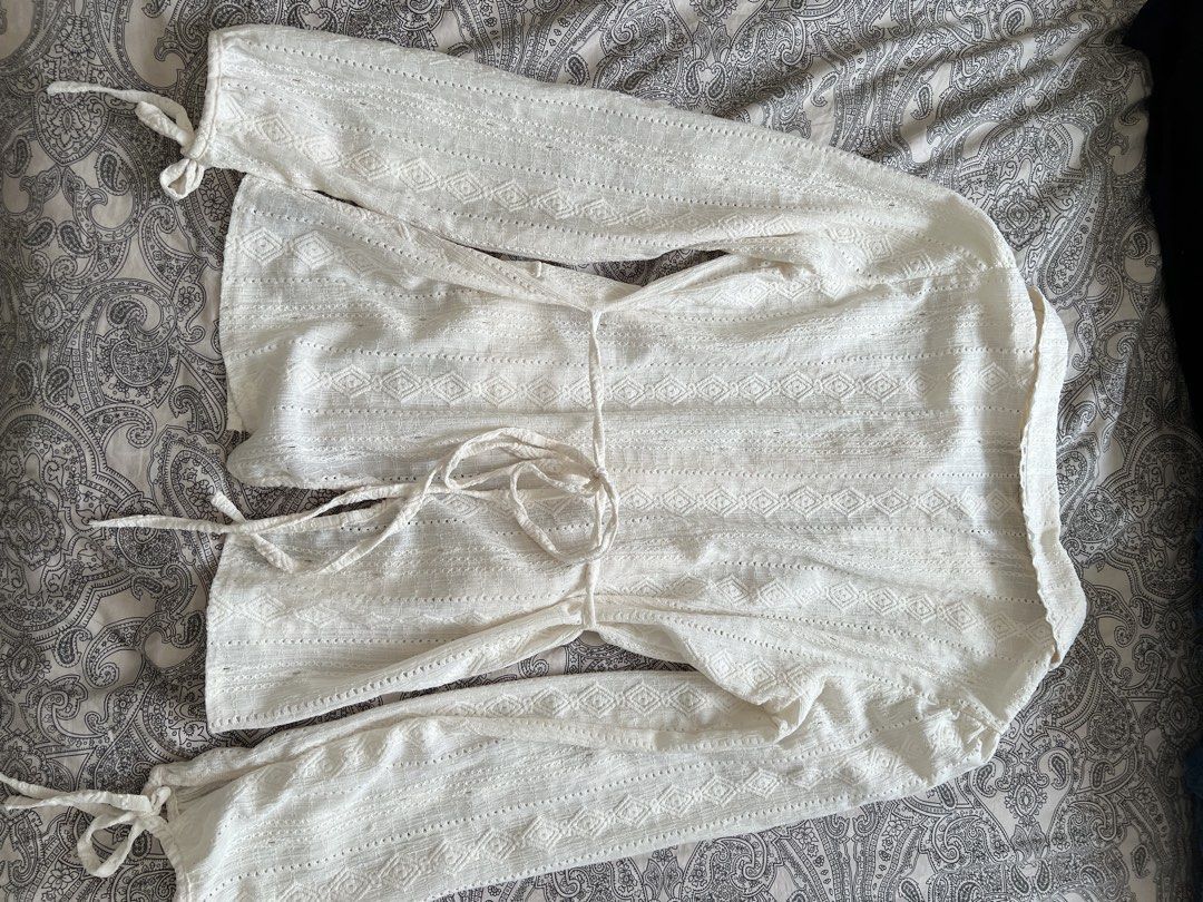 White Lace Button-Up Blouse with Tie Detail (Category: Longsleeves) located in Muntinlupa City. Submitted by sweetlovinnnnn (Listing ID 1463612521, Image 3). Description: - Elegant white long-sleeved blouse - Textured fabric with diamond and stripe patterns - Delicate lace trim on collar and cuffs - Button-up front closure - Adjustable tie details at waist and sleeves - Two functional front pockets - Estimated size: Small to Medium (S/M).