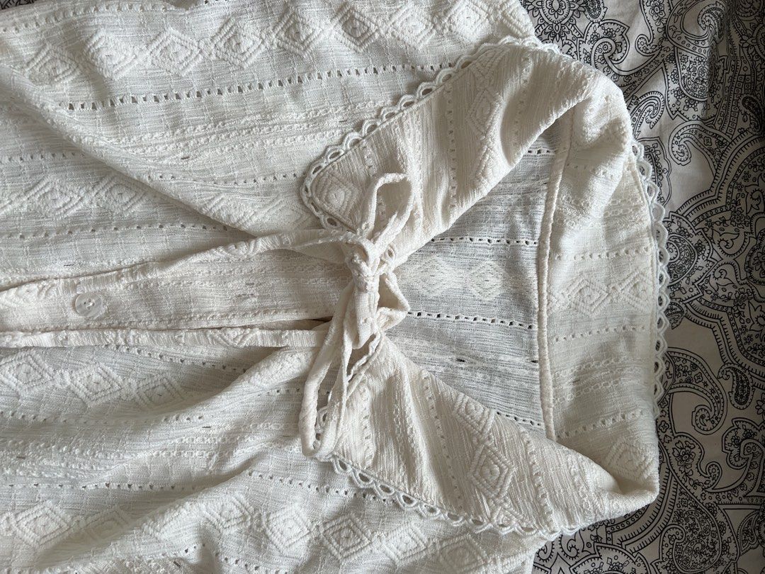 White Lace Button-Up Blouse with Tie Detail (Category: Longsleeves) located in Muntinlupa City. Submitted by sweetlovinnnnn (Listing ID 1463612521, Image 2). Description: - Elegant white long-sleeved blouse - Textured fabric with diamond and stripe patterns - Delicate lace trim on collar and cuffs - Button-up front closure - Adjustable tie details at waist and sleeves - Two functional front pockets - Estimated size: Small to Medium (S/M).
