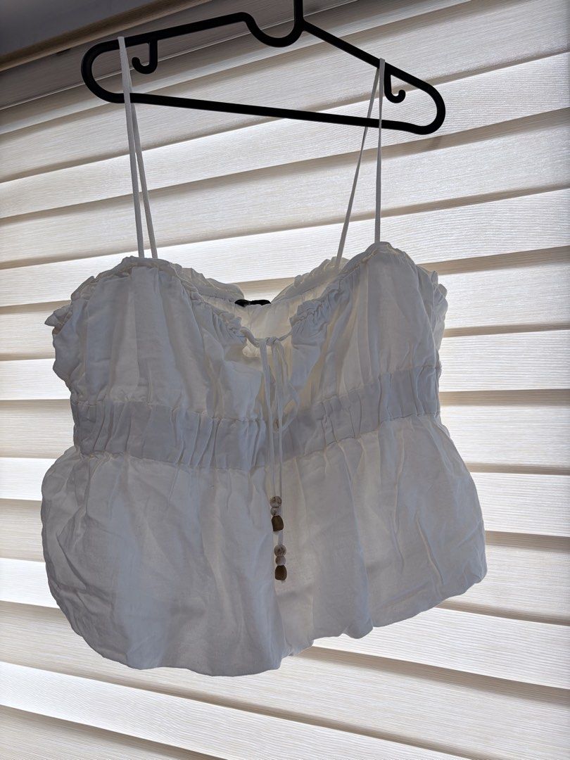 White Ruffle Tie Front Crop Top with Beaded Detail (Category: Sleeveless) located in Manila. Submitted by cheska.closet18 (Listing ID 1463602632, Image 2). Description: - Adorable white crop top - Ruffle trim neckline - Adjustable tie front with wooden beads - Smocked elastic waistband for a comfy fit - Thin, adjustable straps - Versatile: pairs perfectly with high-waisted bottoms - Ideal for summer days and nights out.