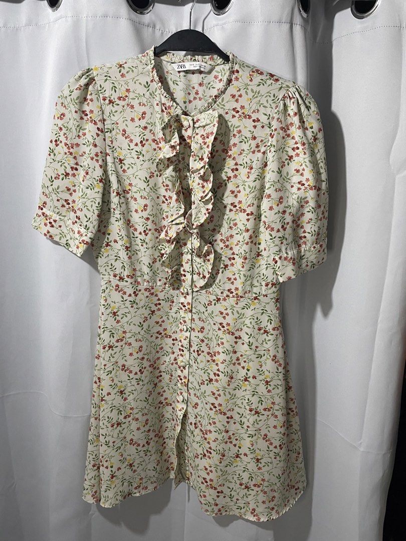 ZARA Floral Ruffle Button-Up Dress (Category: Dresses) located in Bacoor. Submitted by prelovedbyphaty (Listing ID 1463738718, Image 1). Description: - Cream-colored dress - Delicate floral print - Short puff sleeves - Ruffled front with button closures - Slightly flared hem - Ideal for casual wear, picnics, or a day out.