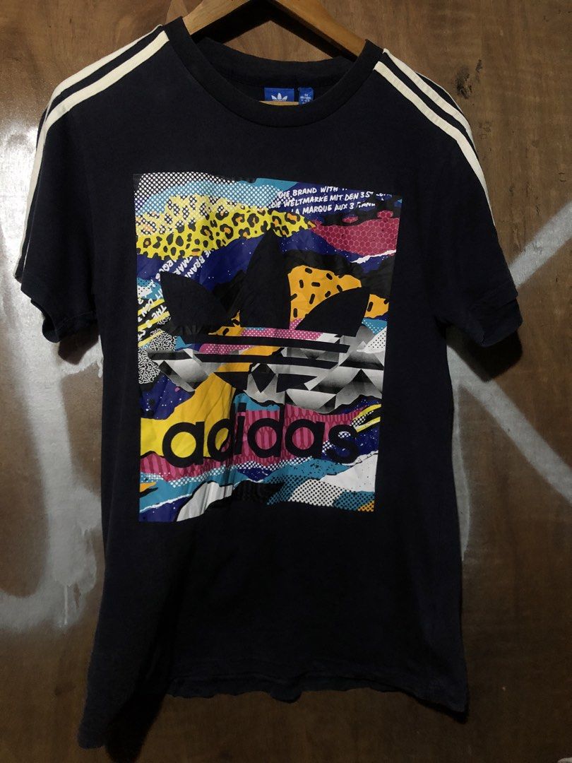 Adidas Graphic T-Shirt (Category: Tshirts & Polo Shirts ) located in Manila. Submitted by bakithrift213 (Listing ID 1463868286, Image 1). Description: - Vibrant abstract graphic print - Classic Adidas logo and three stripes on sleeves - Comfortable fabric for everyday wear - Perfect for casual outfits - Size: Medium (M).