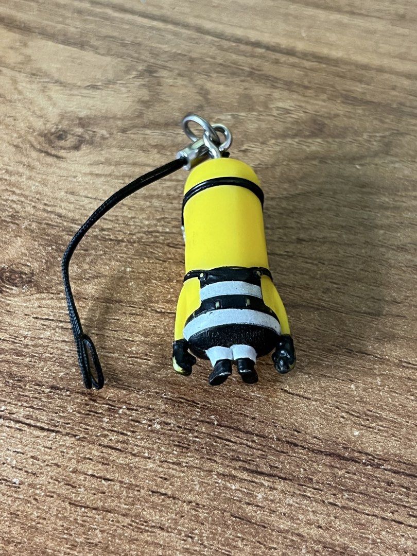 Despicable Me Minion Charm with Strap (Category: Character Goods) located in Gapan. Submitted by lunashop14 (Listing ID 1463749768, Image 2). Description: - Adorable Minion charm from Despicable Me - Features iconic black and white striped outfit - Comes with a convenient black strap and metal clasp - Ideal for personalizing your phone, bag, or keychain - Small and portable accessory for everyday use.