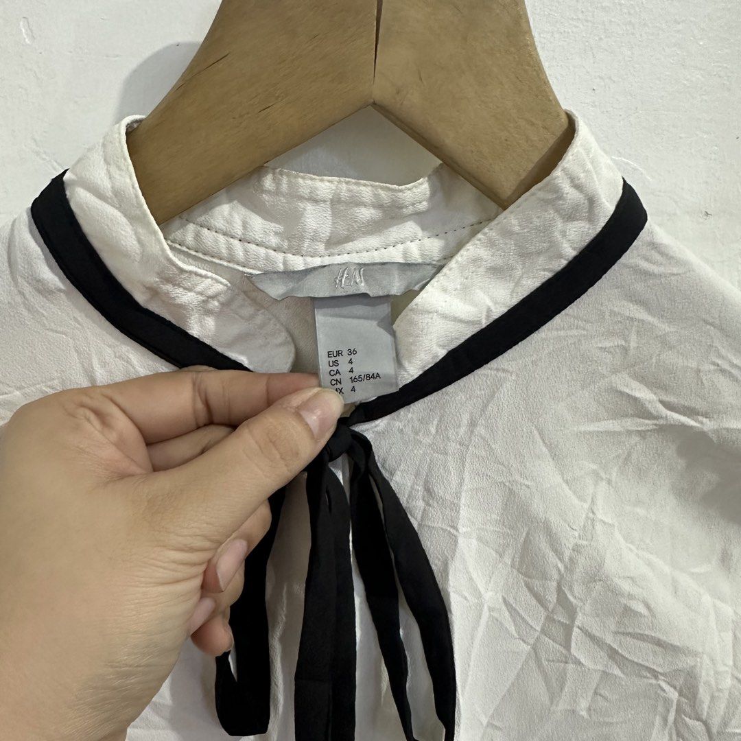 H&M White Long Sleeve Bow Blouse (Category: Longsleeves) located in San Jose del Monte. Submitted by bizzybeebyhgc (Listing ID 1463828570, Image 2). Description: - Brand: H&M - Color: White - Style: Long-sleeved blouse - Features: Black ribbon tie at neck, button-up front, buttoned cuffs - Material: 100% Polyester - Estimated Size: US 4 / EUR 36 - Versatile: Perfect for dressing up or down.