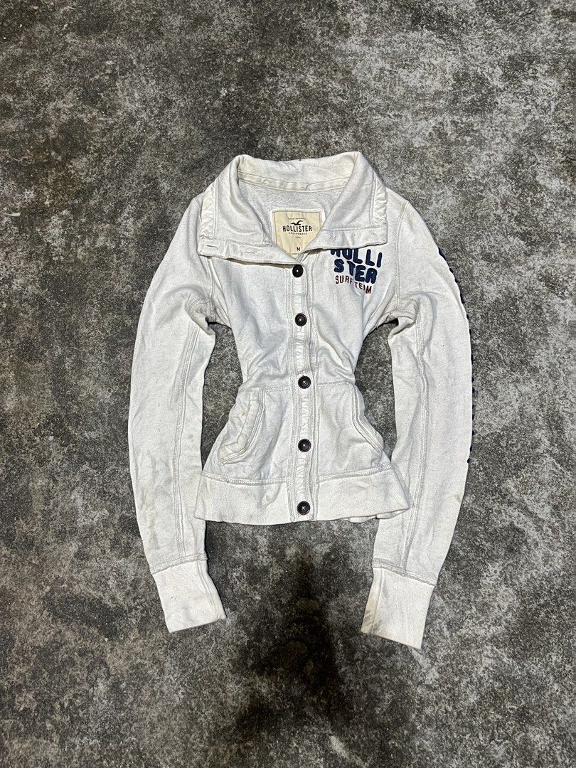 Hollister Surf Team White Button Up Jacket Size M (Category: Coats, Jackets and Outerwear) located in San Isidro, Leyte. Submitted by tigerxdx3580077 (Listing ID 1463880886, Image 1). Description: - White Hollister jacket - 'Hollister Surf Team' graphic - Button-up front - Collared neckline - Long sleeves with ribbed cuffs - Size: Medium (M) - Ideal for casual wear.