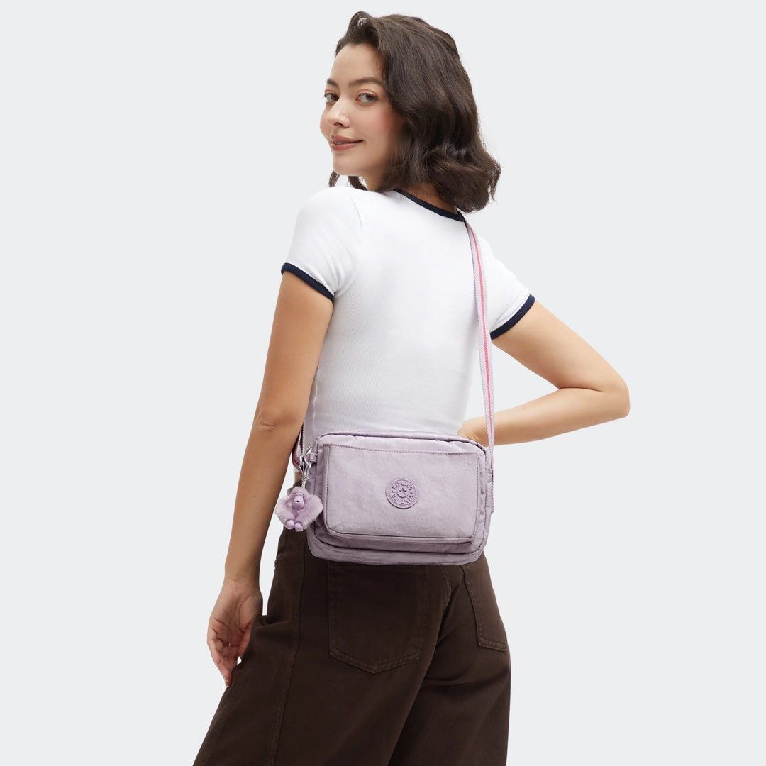 Kipling Abanu Crossbody Bag with Monkey Charm (Category: Cross-body Bags) located in Quezon City. Submitted by cmrls (Listing ID 1462628023, Image 1). Description: - Light purple original Kipling crossbody bag - Brand new with tag still attached - Adjustable strap with pink and white stripes - Secure zipper closure on top - Convenient front flap pocket - Iconic Kipling monkey charm included - Kipling logo prominently displayed on the front.